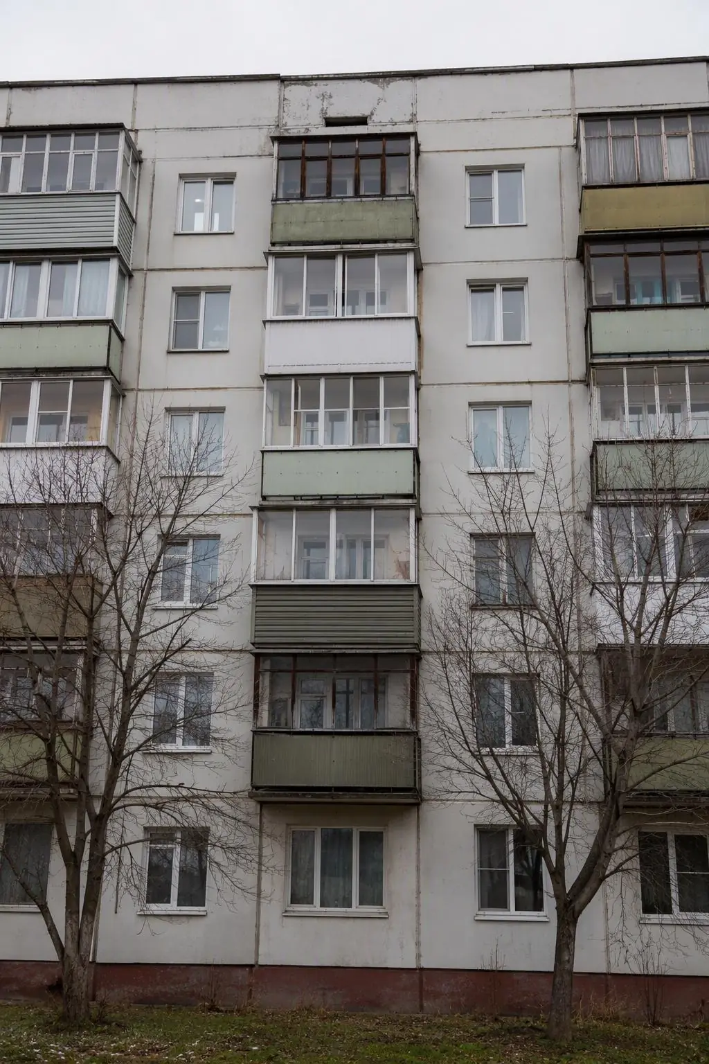 Девятиэтажный панельный дом с балконами, деревья у фасада